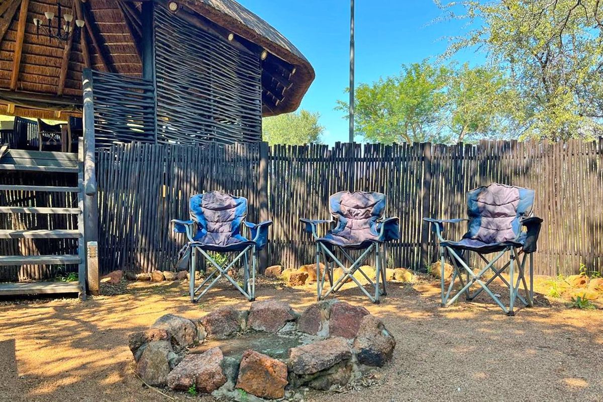 Outdoor rear area featuring a rustic thatched structure with timber cladding, a stone fire pit, and a wooden staircase leading to an elevated deck.