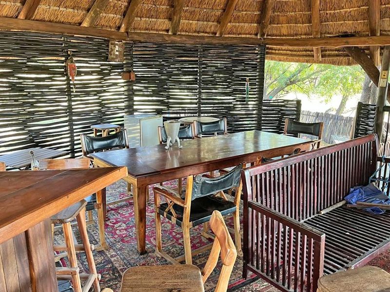A rustic outdoor entertainment area featuring a traditional thatched roof, wattle walling, and a built-in bar counter, ideal for relaxed social gatherings.
