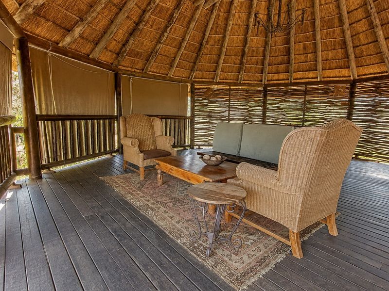 A rustic outdoor patio area featuring a traditional thatched roof, timber decking, and natural wattle screening, providing a comfortable and shaded entertainment space.