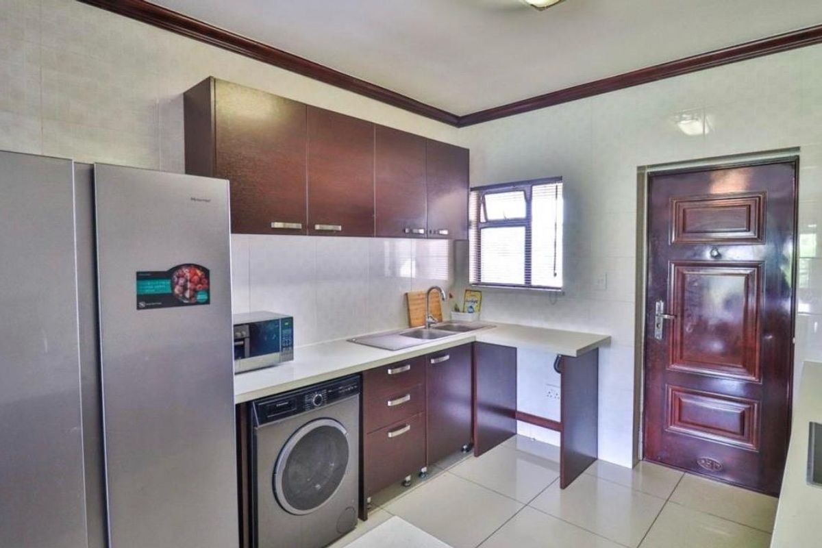 A functional kitchen featuring dark wood cabinetry, laminate countertops, tiled backsplash, and dedicated space for a washing machine.