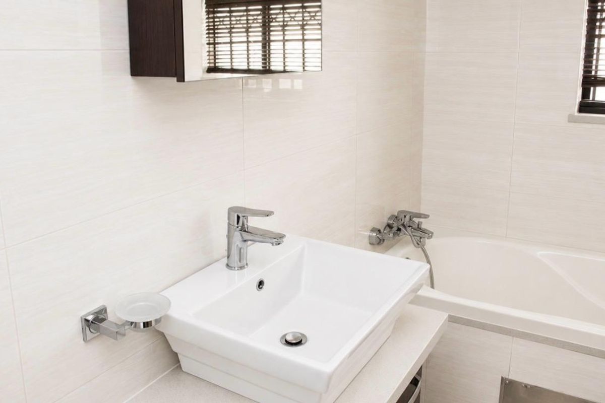 A clean, modern bathroom featuring a wall-mounted basin with chrome mixer tap, built-in bathtub, and neutral wall tiling.