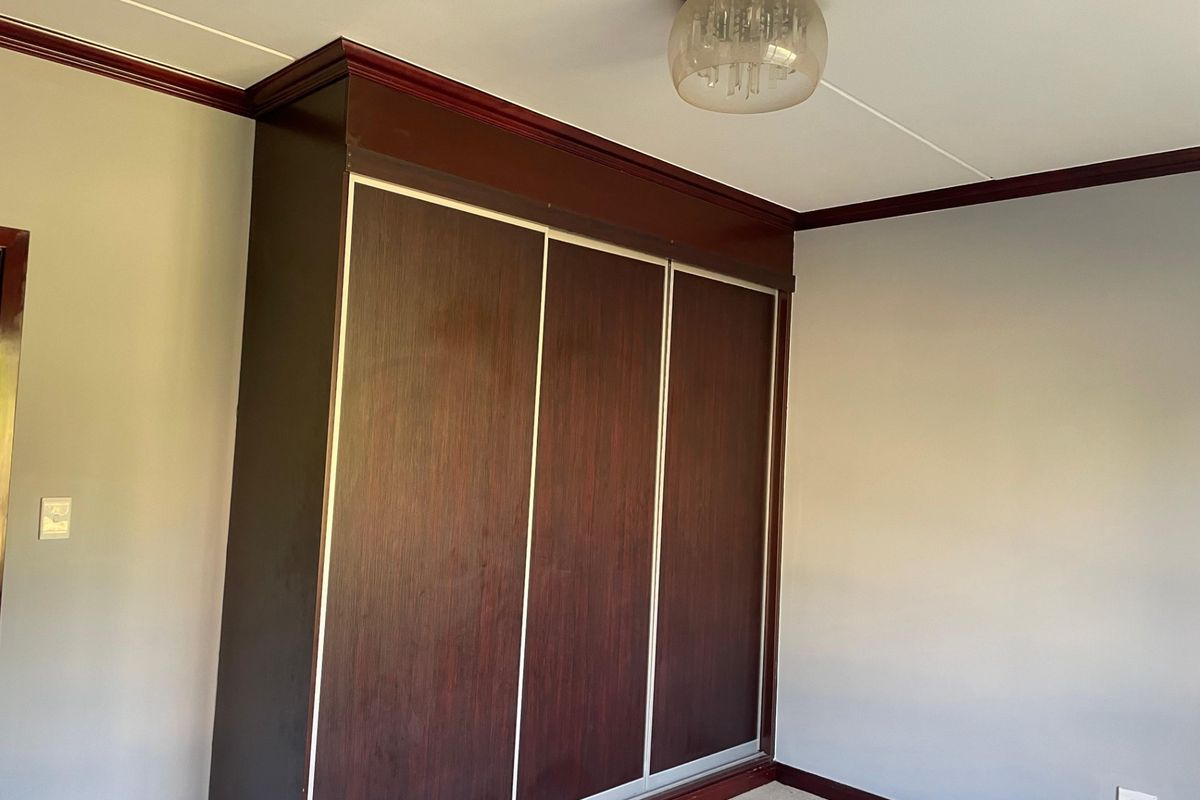 A bedroom featuring dark wood built-in cupboards with sliding doors, complemented by crown molding and a central ceiling light fixture.
