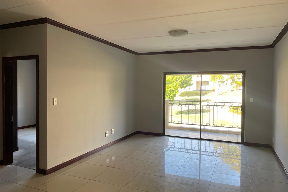 A bright, empty living room featuring polished tile flooring, crown molding, and a sliding glass door leading to a balcony with iron railings.