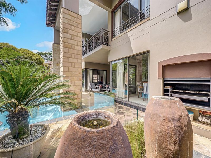 Outdoor entertainment area featuring a swimming pool, built-in braai, and a covered patio with stone accents and glass balustrades.