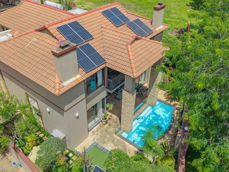 Aerial view of a residential property featuring a tiled roof with solar panels, a swimming pool, and a paved patio area.