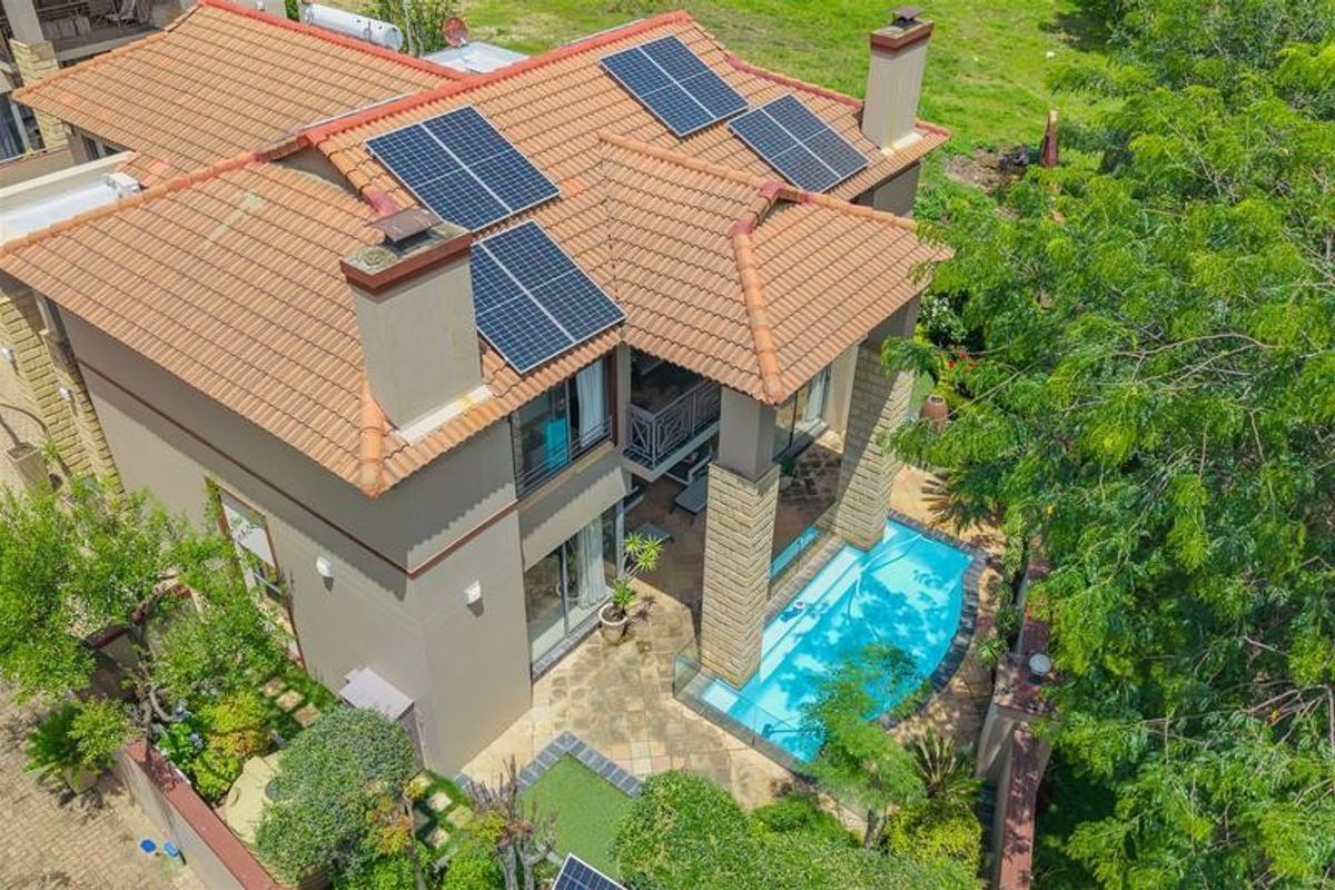 Aerial view of a residential property featuring a tiled roof with solar panels, a swimming pool, and a paved patio area.