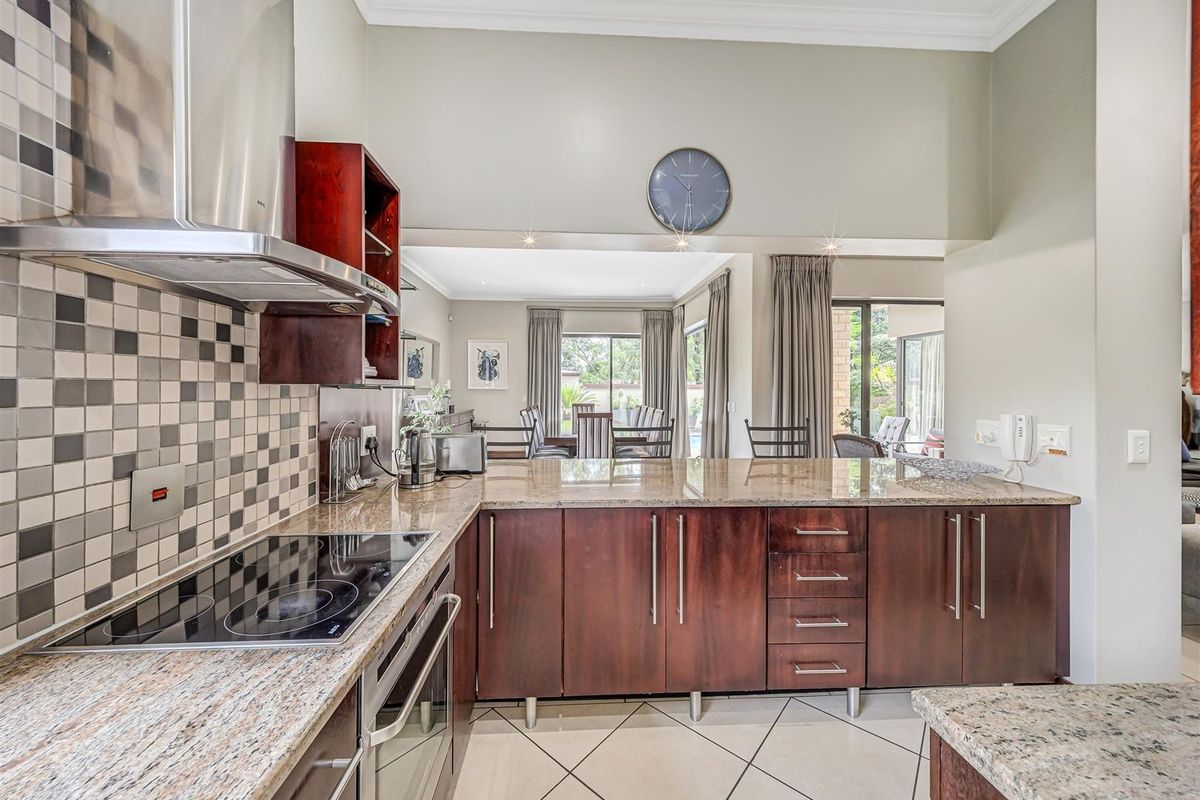Modern kitchen featuring granite countertops, dark wood cabinetry, mosaic backsplash, and integrated appliances, flowing into an open-plan dining and living area.