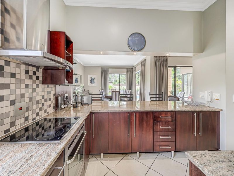 Modern kitchen featuring granite countertops, dark wood cabinetry, mosaic backsplash, and integrated appliances, flowing into an open-plan dining and living area.