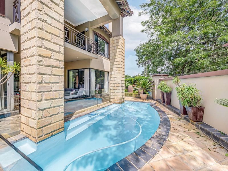 A well-maintained outdoor pool area featuring stone-clad pillars, a glass balustrade, and a paved patio adjacent to a covered ground-floor terrace.