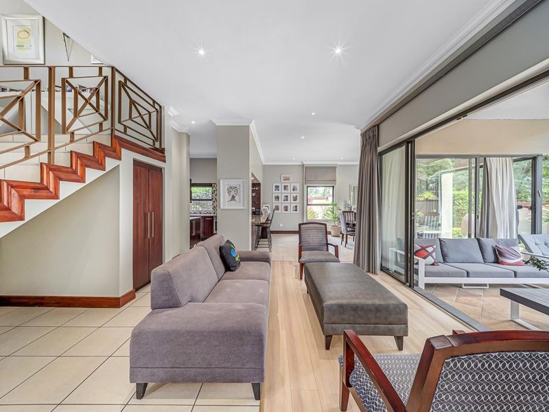 Spacious open-plan living area featuring a modern staircase, large sliding glass doors leading to the patio, and neutral tiled flooring throughout.