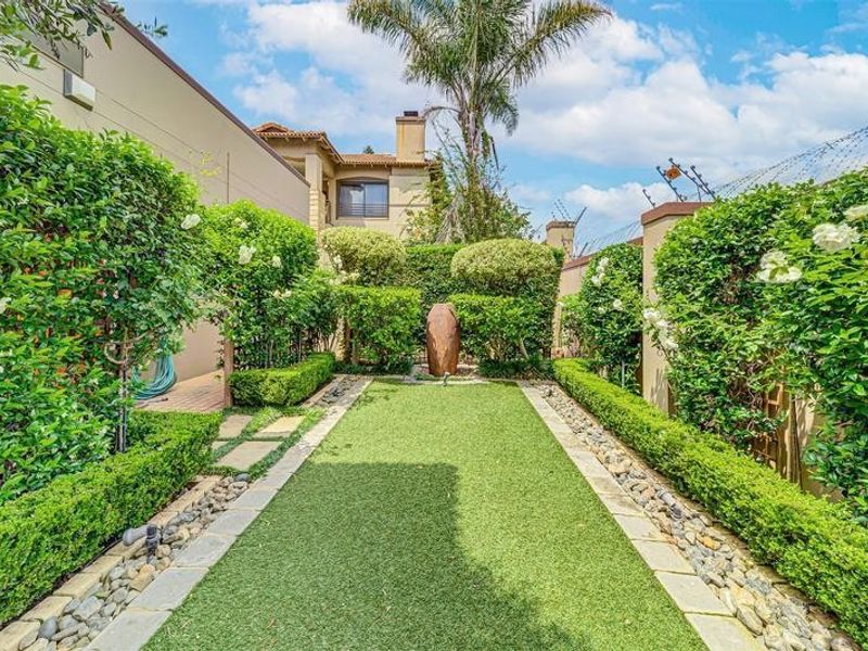A well-maintained private garden featuring artificial lawn, stone pathways, manicured hedges, and secure perimeter walling with electric fencing.