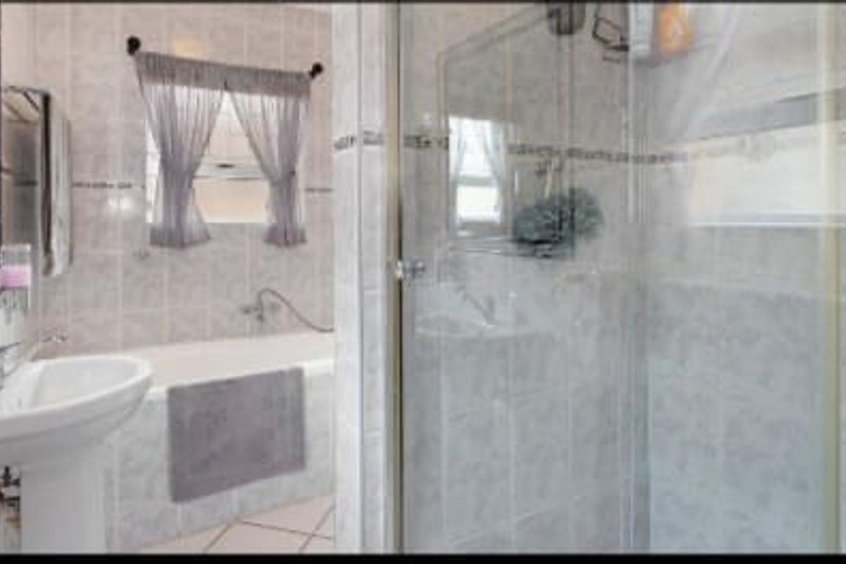 A functional bathroom featuring a pedestal basin, a built-in bathtub, and a separate glass-enclosed shower with neutral ceramic tiling throughout.