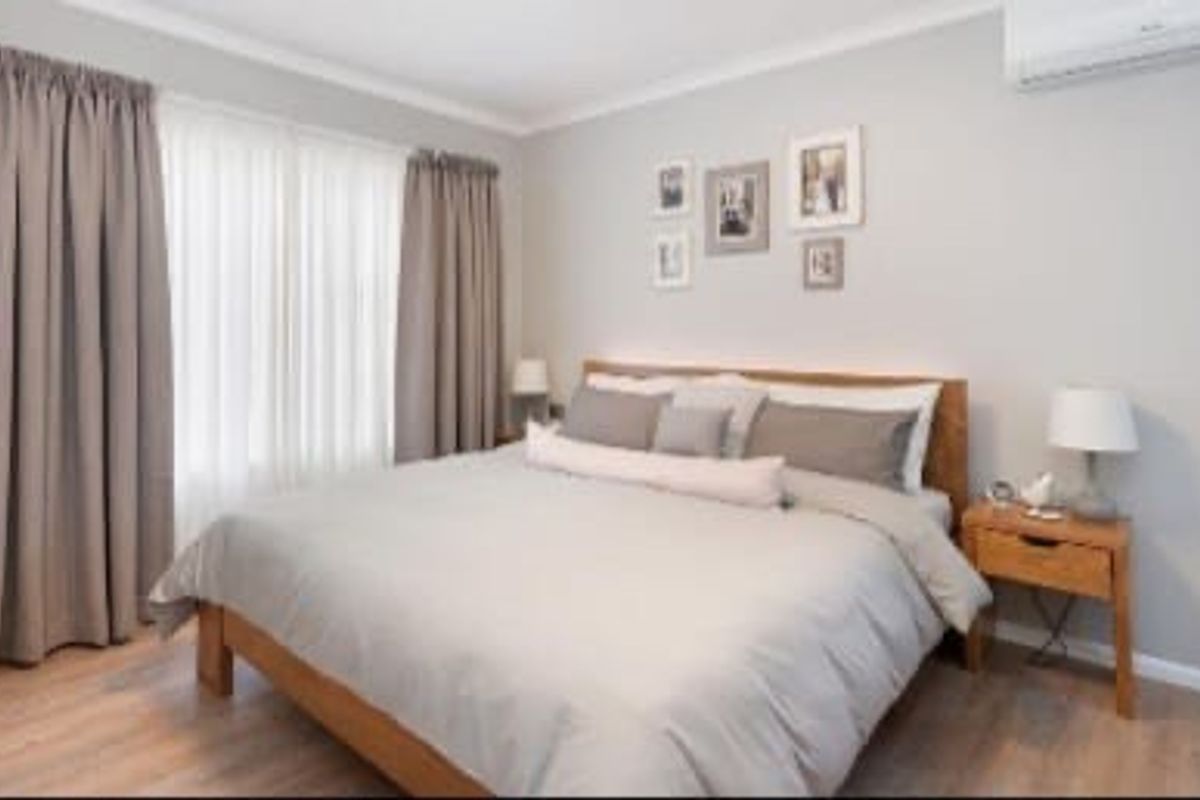 A well-maintained bedroom featuring light laminate flooring, neutral wall tones, and a wall-mounted air conditioning unit.