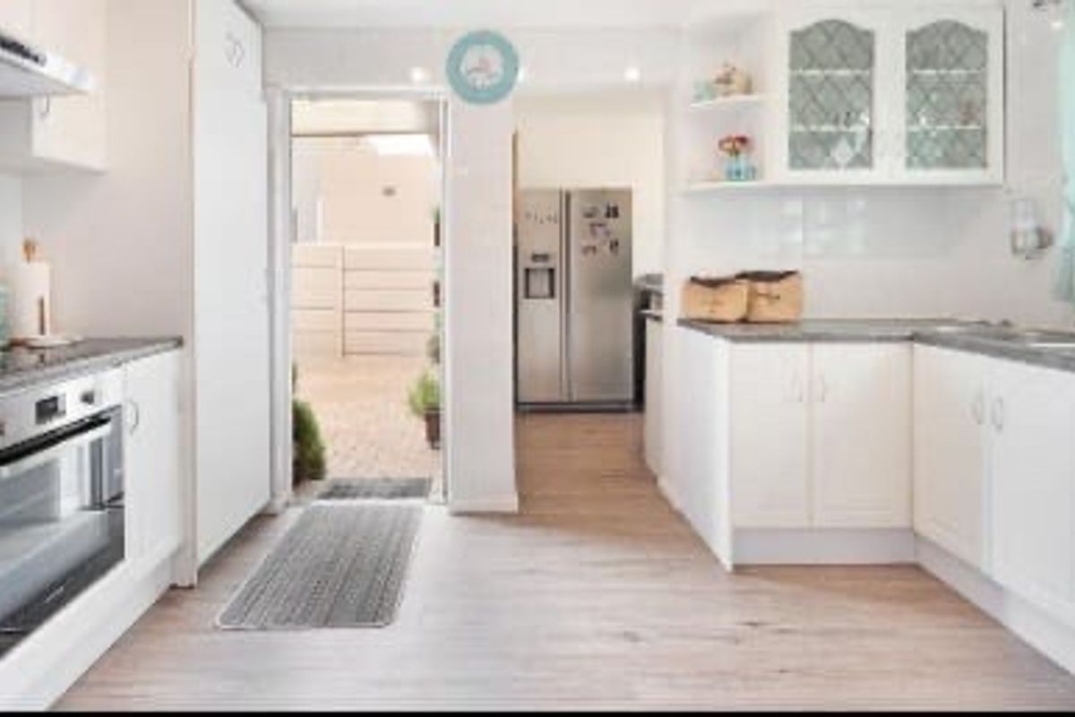 A bright, functional kitchen featuring white cabinetry, laminate countertops, built-in oven, and extractor fan, with direct access to an outdoor patio area.
