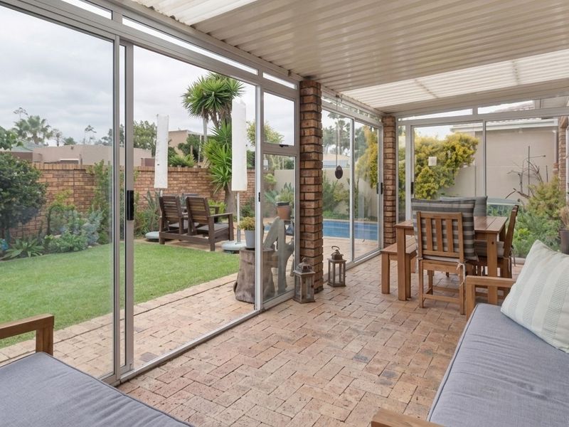 A covered patio area featuring brick paving, brick pillars, and large sliding glass doors that open onto a private garden and pool area.