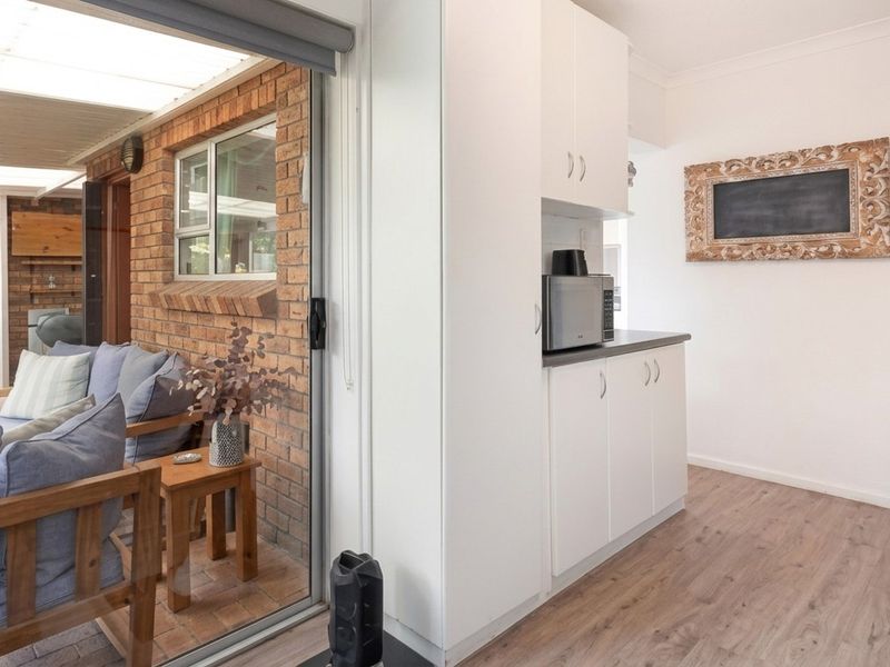 A functional kitchen area featuring white built-in cabinetry and laminate countertops, with direct access to an adjoining covered patio through sliding glass doors.