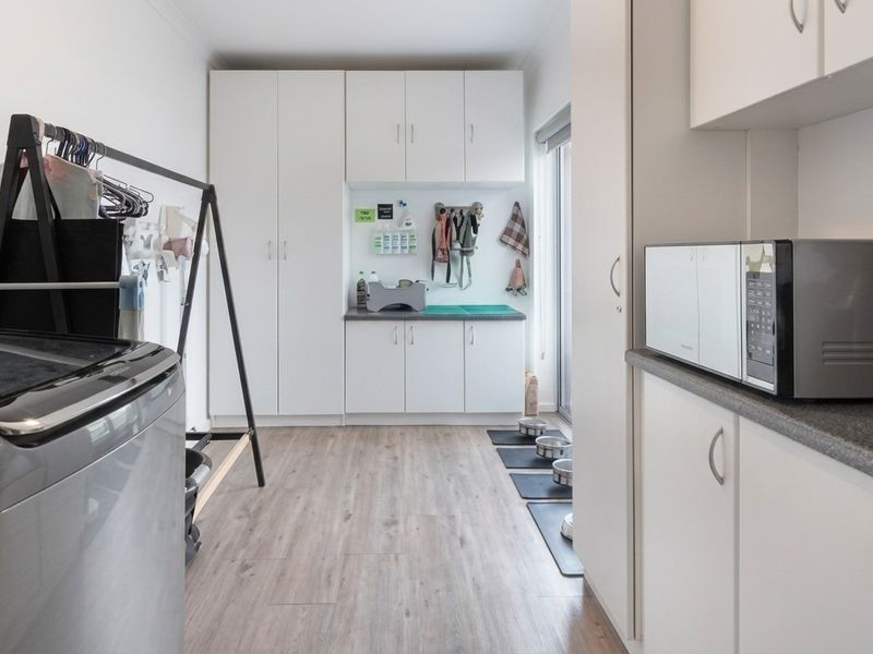 A functional laundry room featuring ample built-in cabinetry, laminate countertops, and durable wood-look flooring with direct access to the exterior.