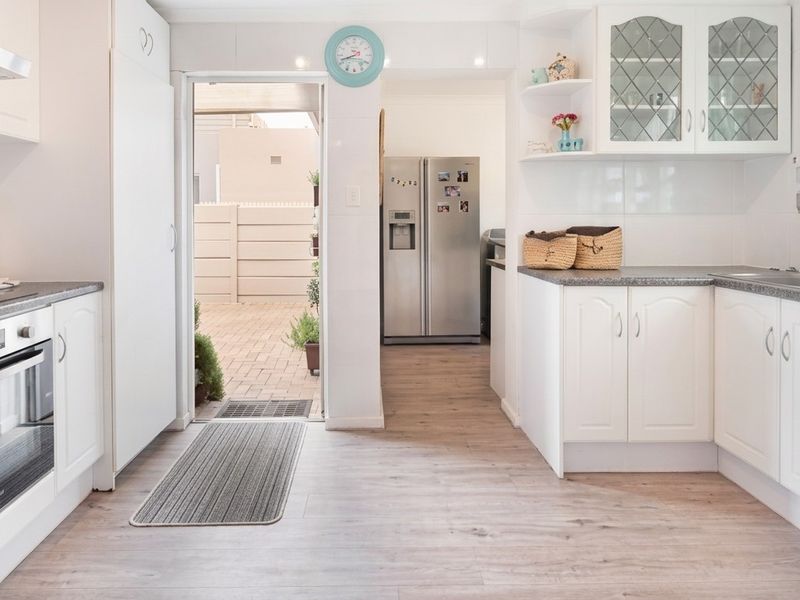 A bright, functional kitchen featuring white cabinetry, laminate flooring, built-in oven, and hob, with direct access to an outdoor paved area.