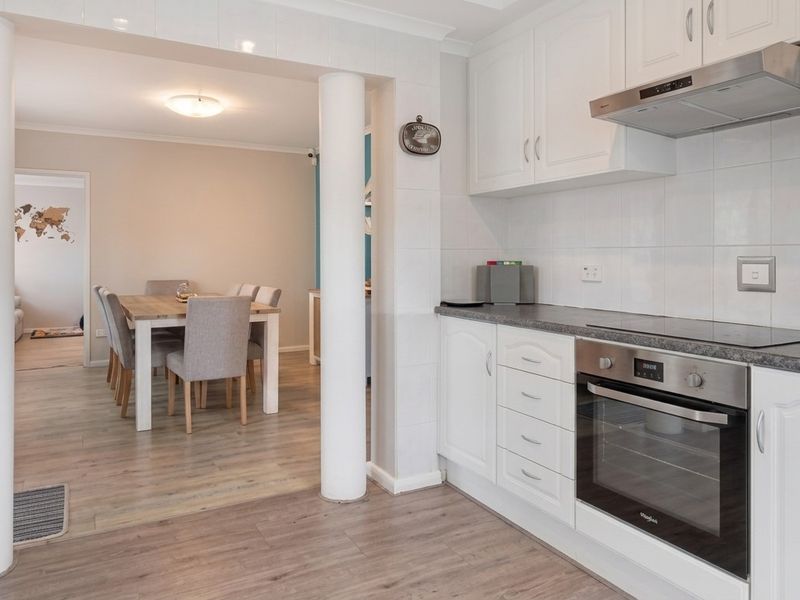 Open-plan kitchen and dining area featuring white cabinetry, integrated appliances, and durable laminate flooring, creating a functional and connected living space.
