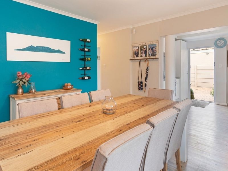A bright dining room featuring laminate flooring, a bold accent wall, and an open-plan layout leading to an outdoor area.