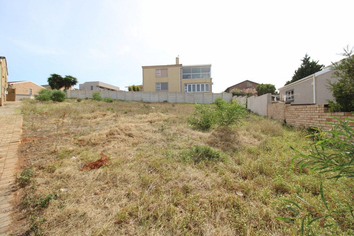 A vacant residential plot featuring a sloped landscape, enclosed by a combination of precast concrete and brick boundary walls.
