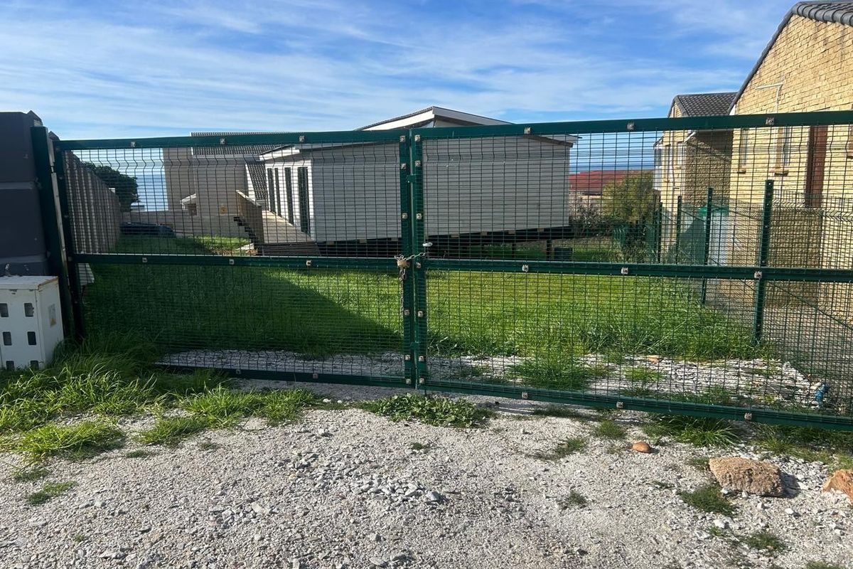A view of a residential property entrance featuring a green metal mesh security gate and a gravel driveway.