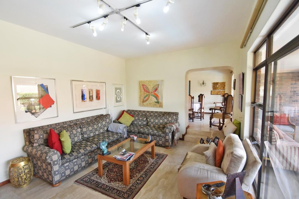 Spacious living room featuring tiled flooring, modern track lighting, and an arched entryway leading to the dining area with access to the patio.