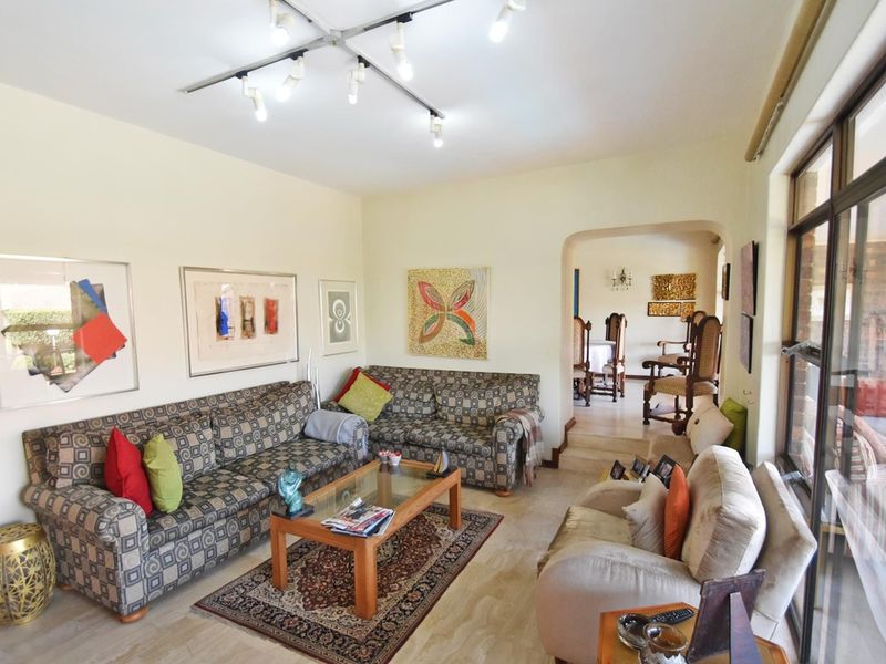 Spacious living room featuring tiled flooring, modern track lighting, and an arched entryway leading to the dining area with access to the patio.