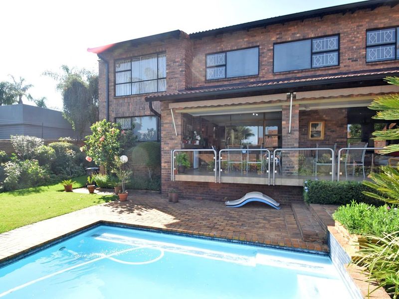 Rear view of a face brick townhouse featuring a swimming pool, paved patio area, and a covered veranda with a glass and steel balustrade.