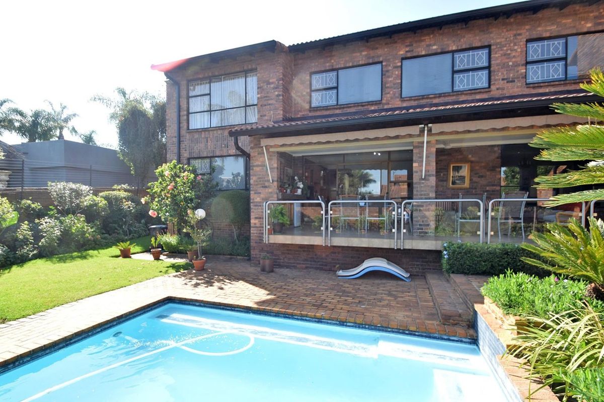 Rear view of a face brick townhouse featuring a swimming pool, paved patio area, and a covered veranda with a glass and steel balustrade.