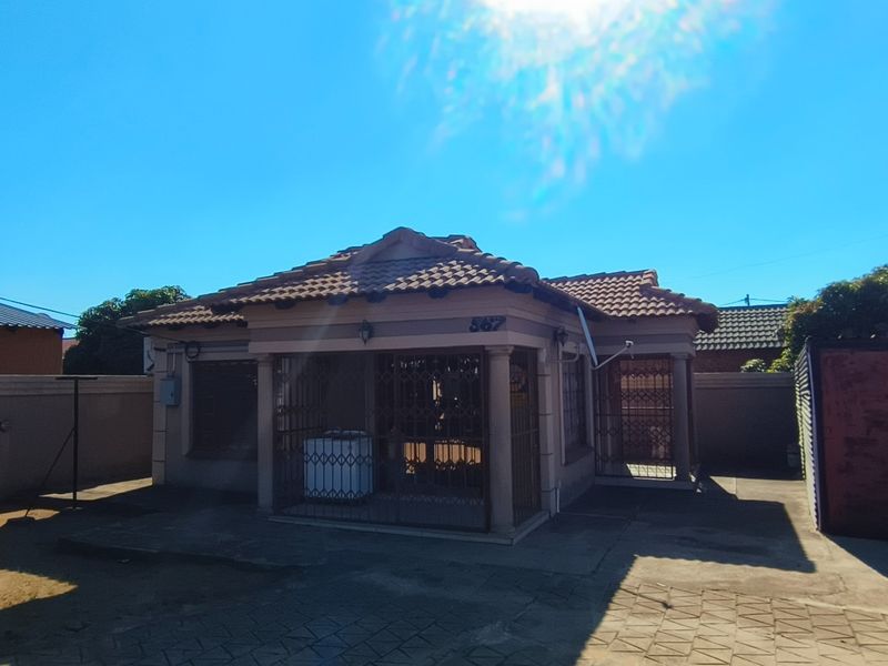 Front view of a single-story house featuring a tiled roof, covered entrance with security gates, and a paved driveway area.