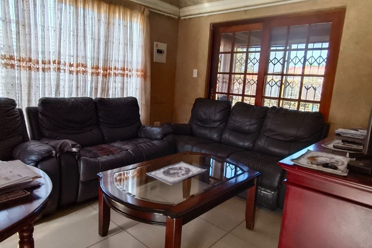 A living room featuring tiled flooring, a sliding glass door with security gate, and dated wall finishes, offering potential for modernization.