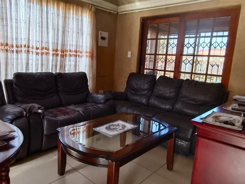 A living room featuring tiled flooring, a sliding glass door with security gate, and dated wall finishes, offering potential for modernization.