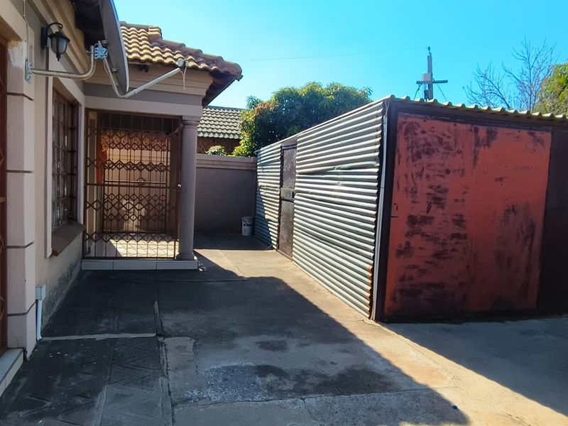 Rear exterior area featuring concrete paving, a security gate, and a corrugated metal structure showing signs of wear and corrosion.