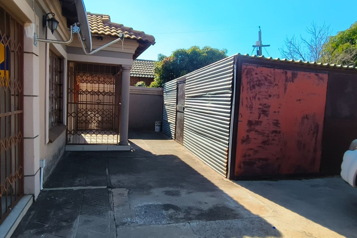 Rear exterior area featuring concrete paving, a security gate, and a corrugated metal structure showing signs of wear and corrosion.