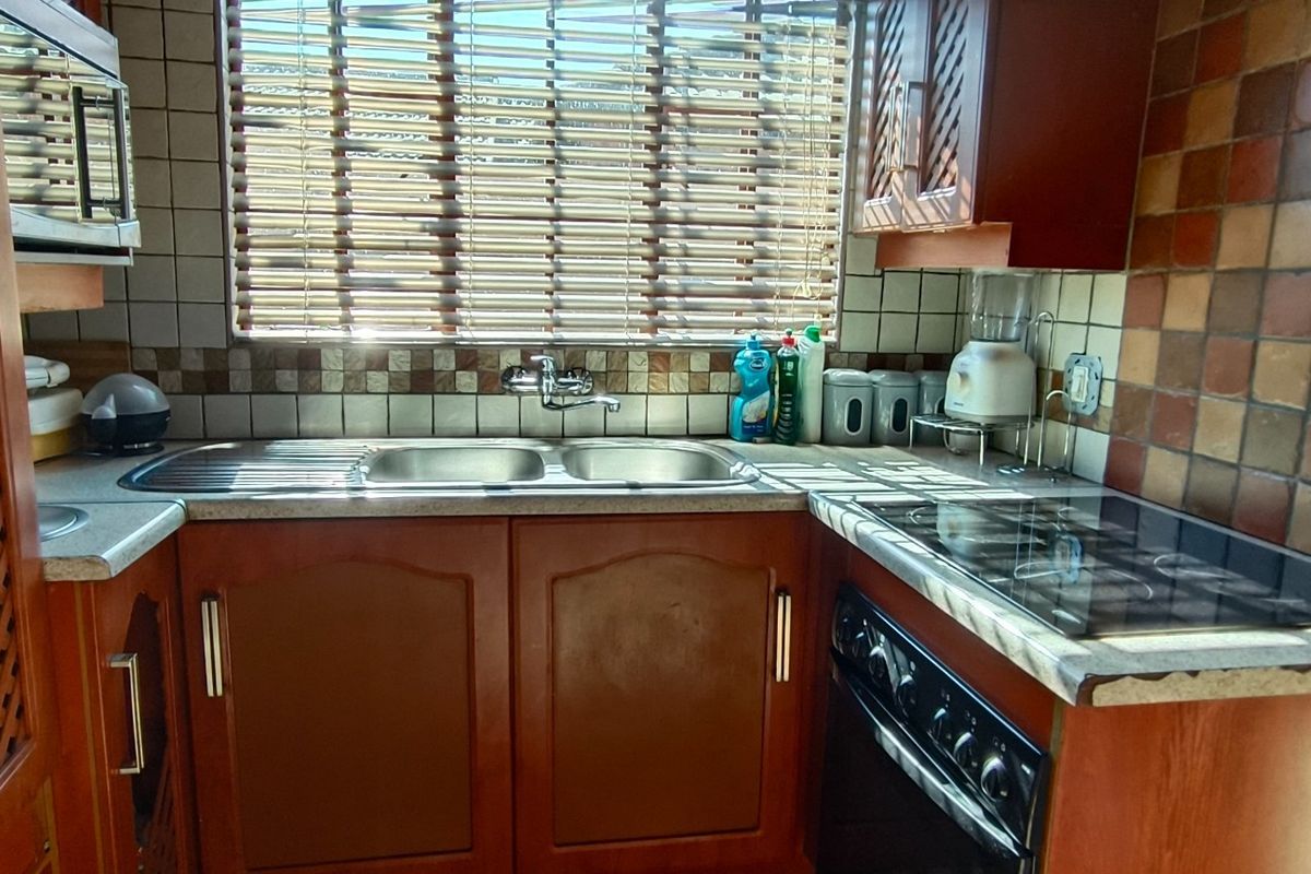 A compact kitchen featuring wooden cabinetry, a double sink, built-in oven with electric hob, and a tiled backsplash.