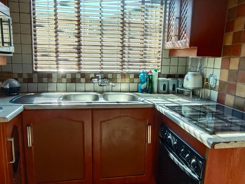 A compact kitchen featuring wooden cabinetry, a double sink, built-in oven with electric hob, and a tiled backsplash.