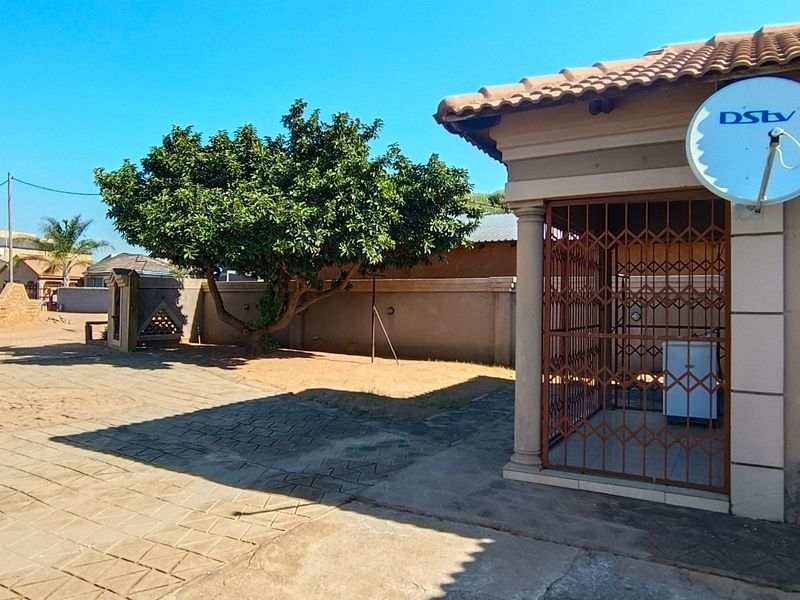 Front exterior view of the property featuring a paved driveway, perimeter wall, and a secure entrance area with a satellite dish installed.