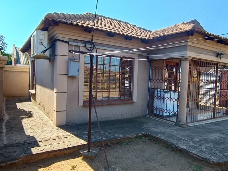 Front elevation of a single-story house featuring a tiled roof, security bars on windows and porch, and a paved driveway area.