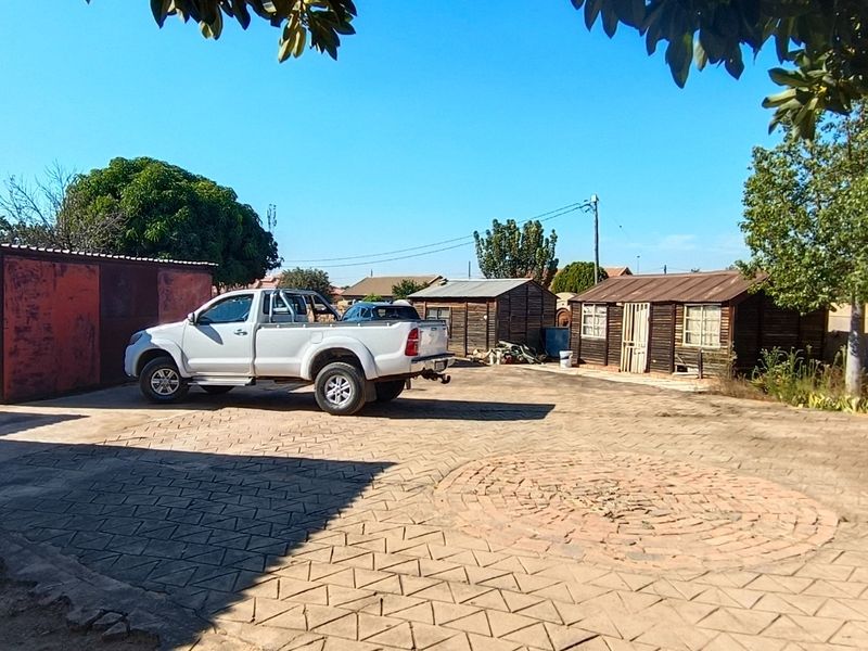 Spacious paved front yard area featuring a metal garage structure, additional timber outbuildings, and secure gated access.