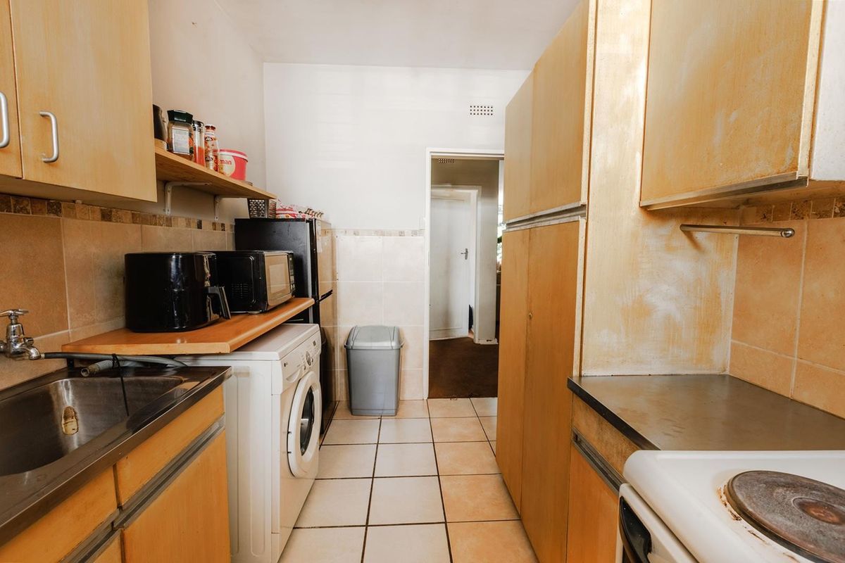 A functional kitchen featuring built-in wooden cabinetry, tiled flooring, a stainless steel sink, and an electric stove, offering potential for modernization.