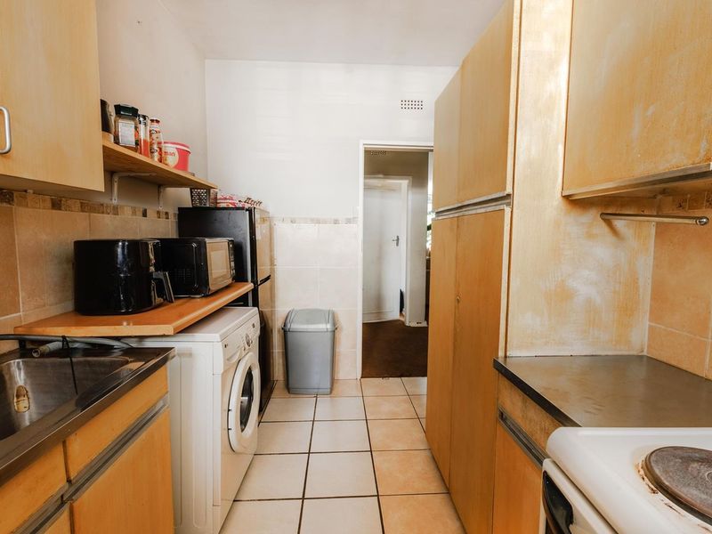 A functional kitchen featuring built-in wooden cabinetry, tiled flooring, a stainless steel sink, and an electric stove, offering potential for modernization.