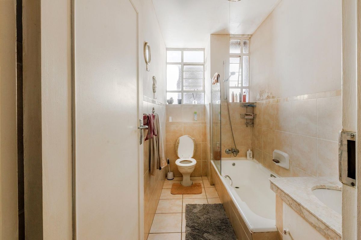 A compact bathroom featuring a bathtub with a glass screen, a toilet, and a vanity sink, with tiled finishes throughout.