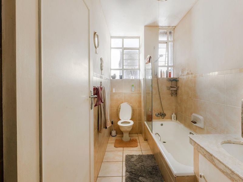 A compact bathroom featuring a bathtub with a glass screen, a toilet, and a vanity sink, with tiled finishes throughout.