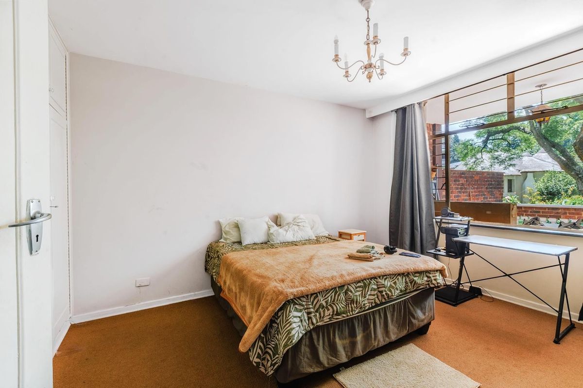 A bedroom featuring built-in cupboards, large windows providing natural light, and carpet flooring. The space offers a functional layout ready for updates.