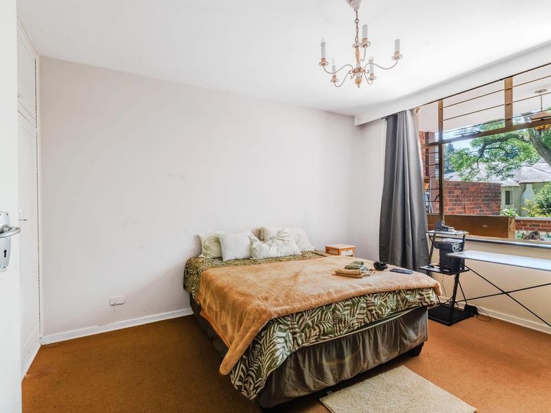 A bedroom featuring built-in cupboards, large windows providing natural light, and carpet flooring. The space offers a functional layout ready for updates.