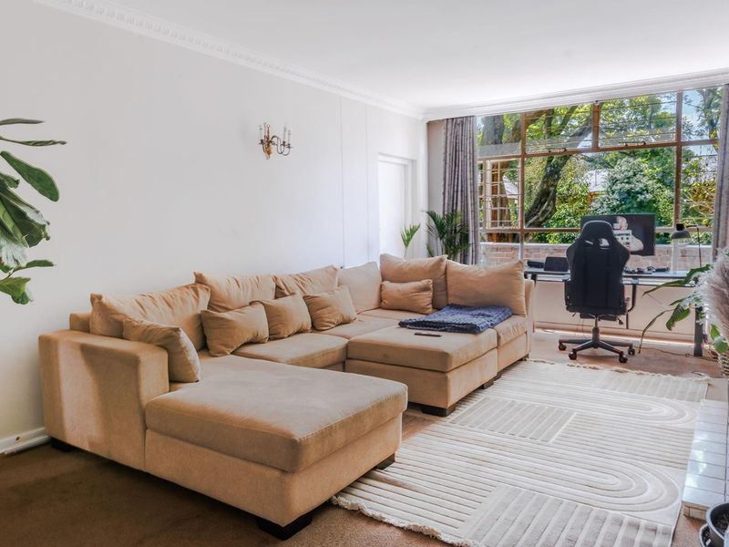 A bright and spacious living room featuring large windows that provide natural light and a pleasant view of the surrounding greenery.