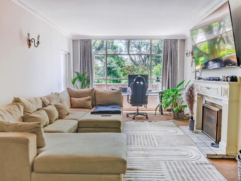A comfortable living room featuring a classic fireplace with a mantelpiece, crown molding, and a large window providing natural light and garden views.