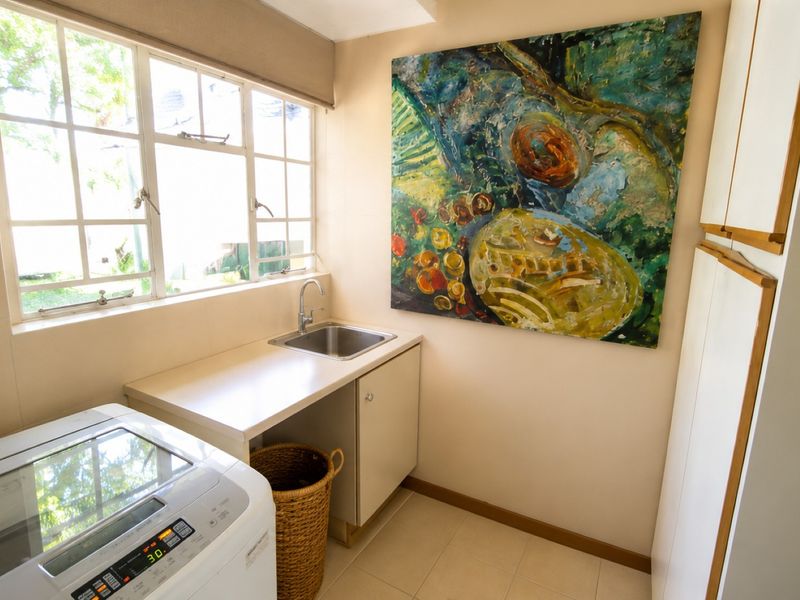 A functional laundry room featuring a stainless steel sink, built-in cabinetry, laminate countertop, and tiled flooring with natural light from casement windows.