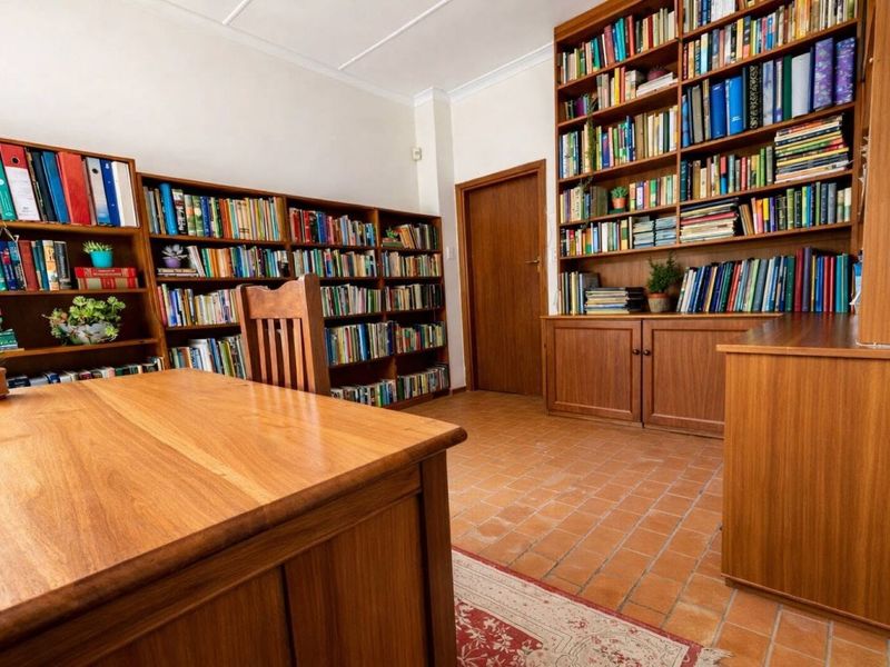A dedicated home office featuring extensive built-in wooden shelving, terracotta tile flooring, and a warm, functional workspace layout.